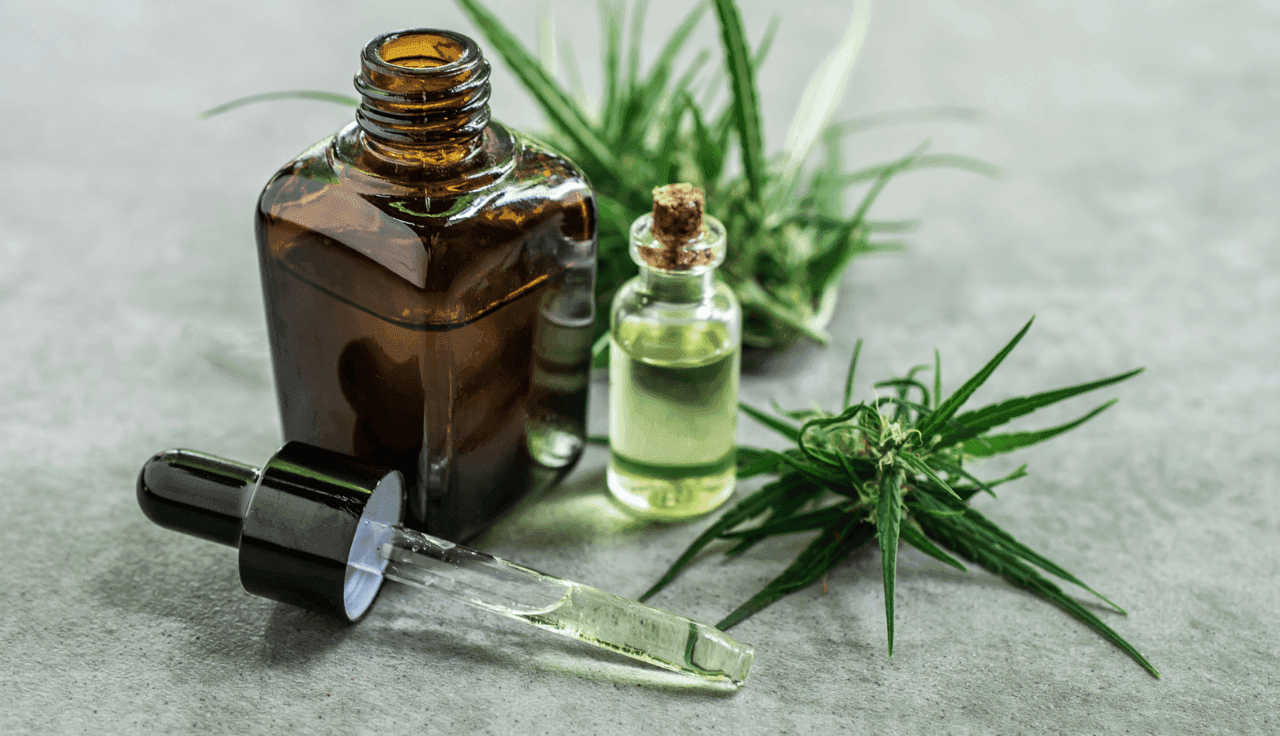 Cannabis-Extrakt in 2 Pipettenflaschen, umgeben von Cannabis-Blättern.